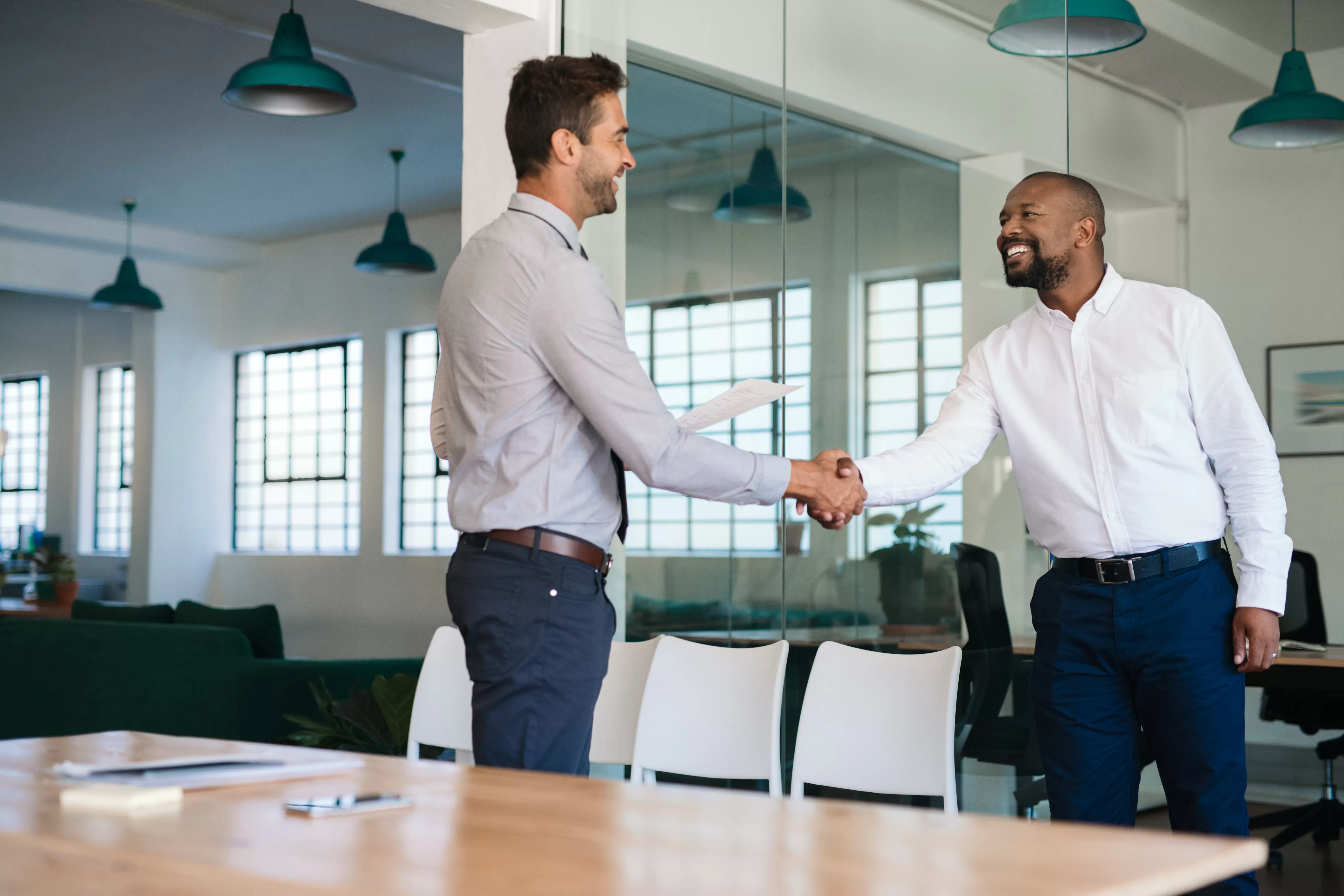 A man confidently shakes a car salesman's hand after negotiating a great purchase price