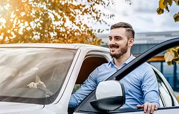 A man is smiling as he gets into his car after getting lower monthly payments with an auto refinance.