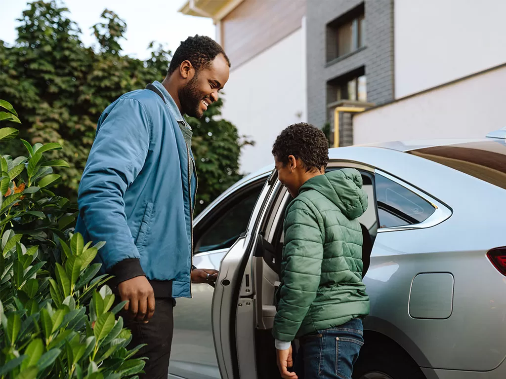 A father helps his young son into the new car he financed with a credit union auto loan.