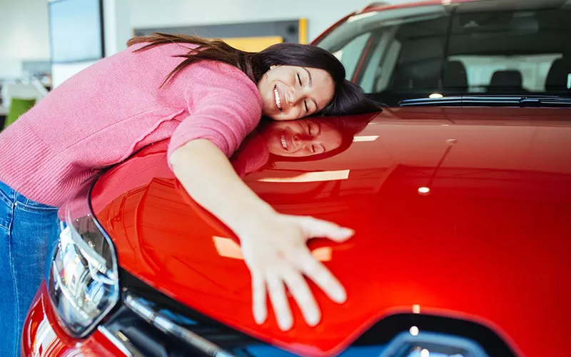 A lady excitedly giving a hug to the new car she just purchased at the dealership.